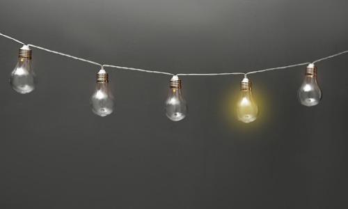"garland of lightbulbs with one glowing on gray background"