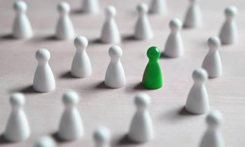 "green pawn amid white pawns against white background"