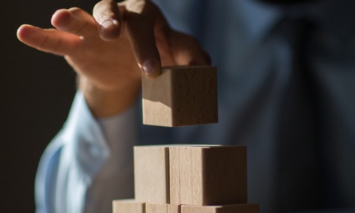 "hand placing wooden blocks on top of one another"