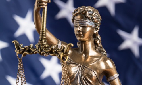 "statue of blindfolded Lady Justice in front of American flag"