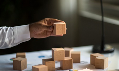 "hand holding a wooden block, stacking on top of other wooden blocks"