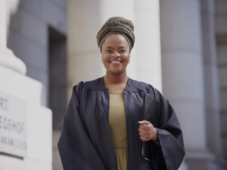 Portrait of a confident Black woman dressed in a judicial robe, standing in a courthouse setting and smiling with poise and authority, representing empowerment, justice and leadership.