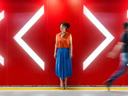 A woman standing between arrows pointing in different directions while someone walks past.