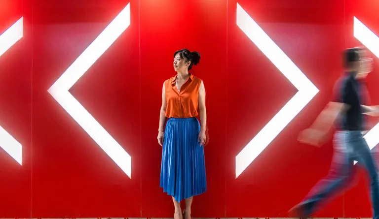 A woman standing between arrows pointing in different directions while someone walks past.