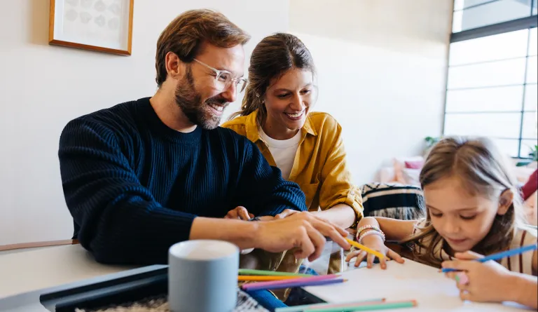 Family sitting together at a table while daughter colors