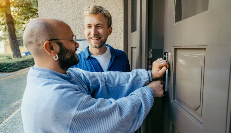 Two men unlocking a door together.
