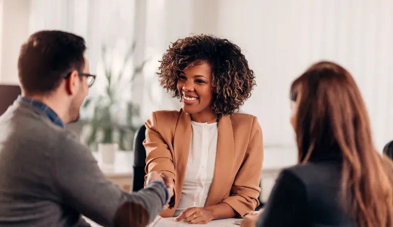 A woman shakes the hands of the man and woman at her desk