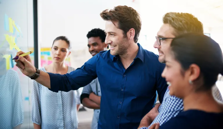 A man surrounded by a group of people draws on a whiteboard.
