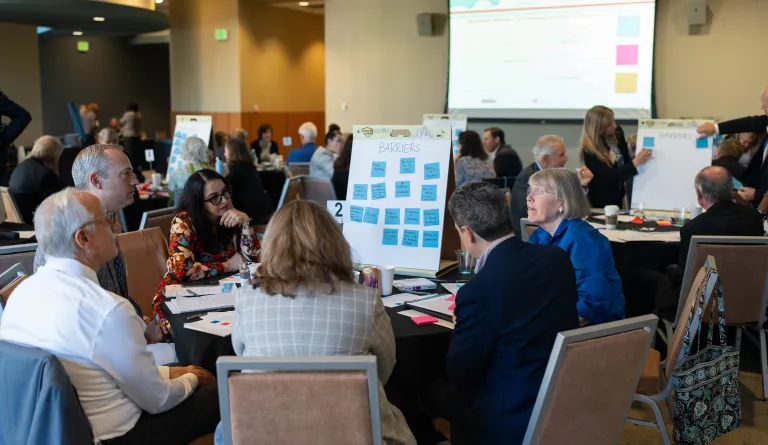 Multiple tables across a conference room work on solving problems at an IAALS judicial convening.