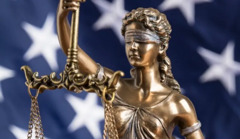 statue of blindfolded Lady Justice in front of American flag