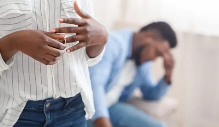 woman in foreground taking off wedding ring while man in background has head in hands