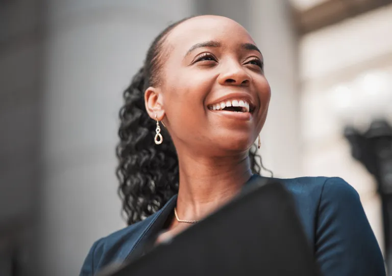 Portrait of a professional Black woman in a tailored dark suit, smiling thoughtfully with her head slightly tilted and her eyes gazing into the distance, conveying confidence, empowerment, and readiness to lead in a legal or corporate setting.