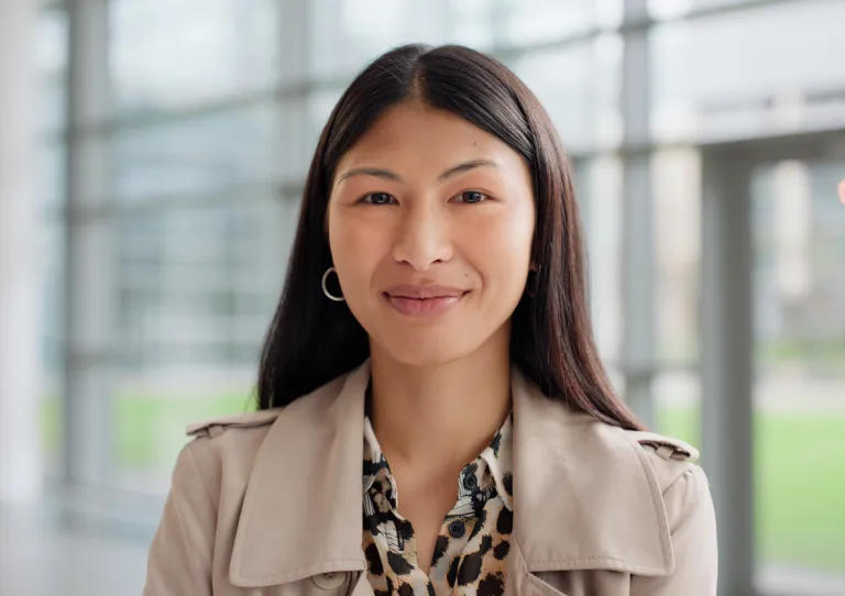 Portrait of a confident Asian woman in a dark blazer, smiling warmly at the camera with arms crossed, exuding professionalism and pride in her legal or corporate career.