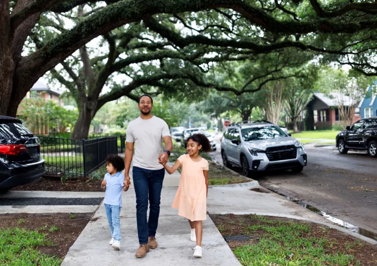 A proud father walking down a city street with his two children, a son and a daughter, holding hands and smiling together.