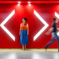 A woman standing between arrows pointing in different directions while someone walks past.