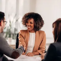 A woman shakes the hands of the man and woman at her desk