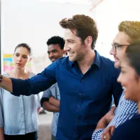A man surrounded by a group of people draws on a whiteboard.