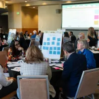 Multiple tables across a conference room work on solving problems at an IAALS judicial convening.