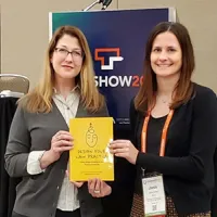 two women standing next to each other holding yellow book
