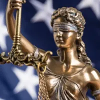 statue of blindfolded Lady Justice in front of American flag