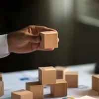 hand holding a wooden block, stacking on top of other wooden blocks