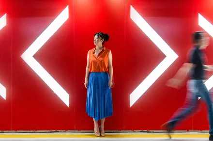 A woman standing between arrows pointing in different directions while someone walks past.