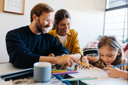 Family sitting together at a table while daughter colors