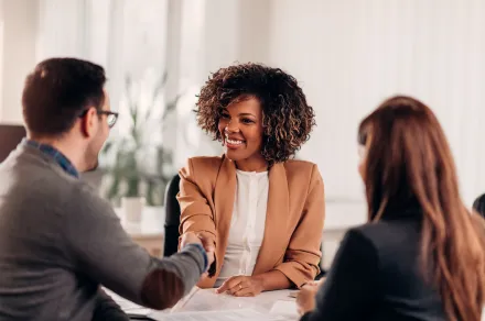 A woman shakes the hands of the man and woman at her desk