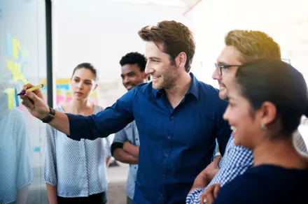 A man surrounded by a group of people draws on a whiteboard.