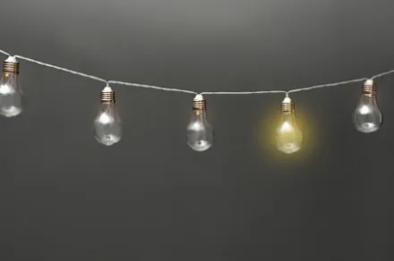 garland of lightbulbs with one glowing on gray background