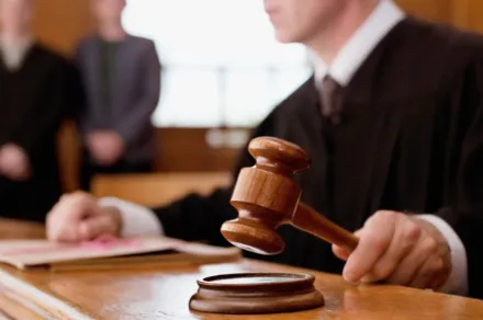 Judge, wearing black robes and whose face is out of frame, hitting a gavel