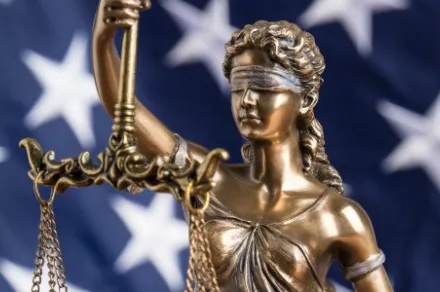 statue of blindfolded Lady Justice in front of American flag