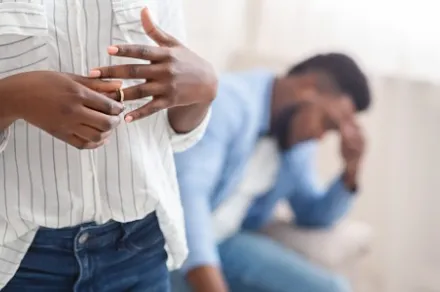 woman in foreground taking off wedding ring while man in background has head in hands