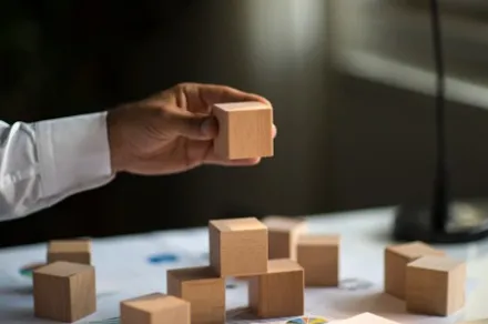 hand holding a wooden block, stacking on top of other wooden blocks